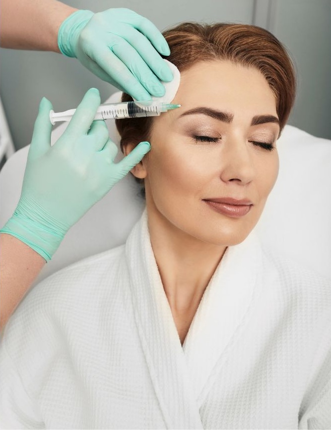 Woman in a white robe with her eyes closed receiving facial injections