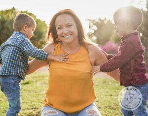 Mother outside enjoying nature, kneeling down in between her two toddler boys