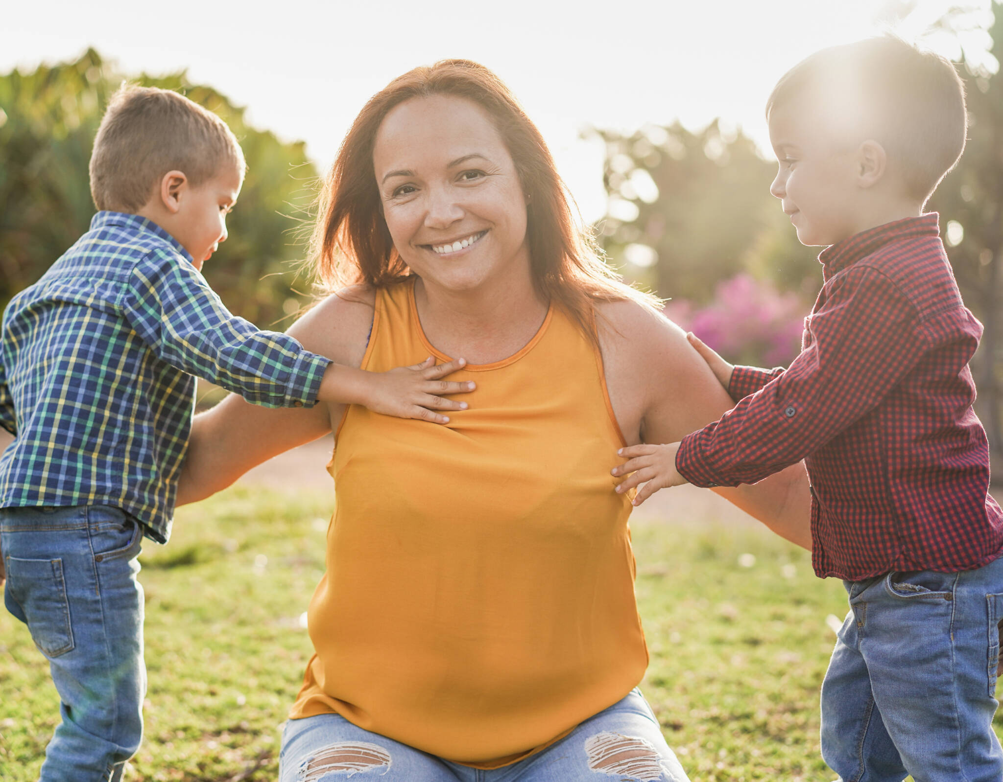 Mother outside enjoying nature, kneeling down in between her two toddler boys