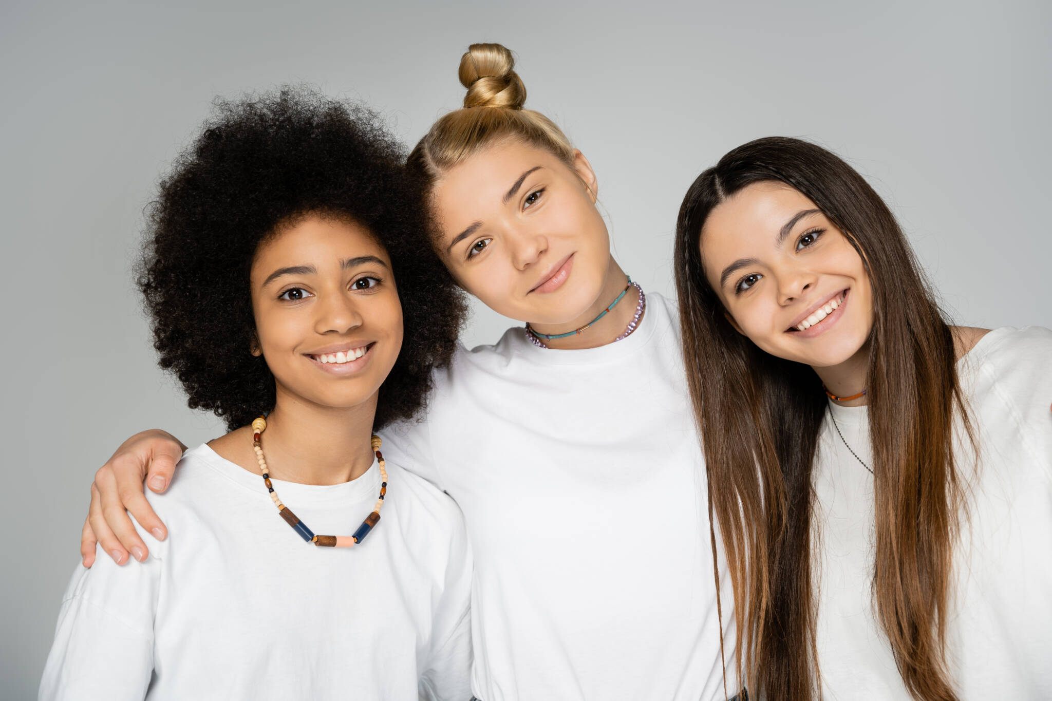 Three multi-ethnic teenage girls smiling and embracing each other